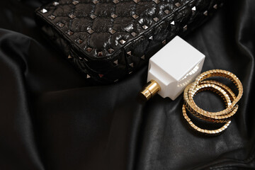 Leather bag, bottle of perfume and golden bracelets on black fabric, closeup. Space for text