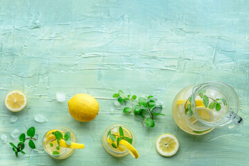 Lemonade with mint. Lemon water drink with ice. Two glasses and a pitcher on a blue background, shot from the top with copy space. Detox beverage. Fresh homemade cocktail