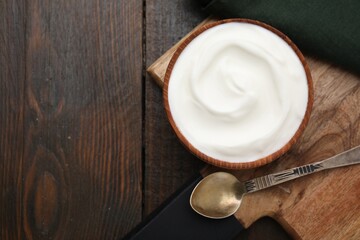Delicious natural yogurt in bowl and spoon on wooden table, top view. Space for text