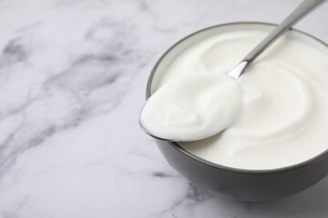 Delicious natural yogurt in bowl and spoon on white marble table, closeup. Space for text