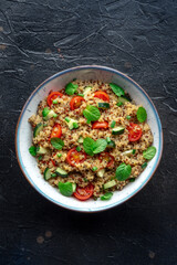 Quinoa tabbouleh salad in a bowl, a healthy dinner with tomatoes and mint, top shot on black