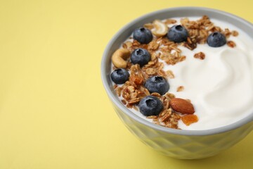 Bowl with yogurt, blueberries and granola on yellow background, closeup. Space for text