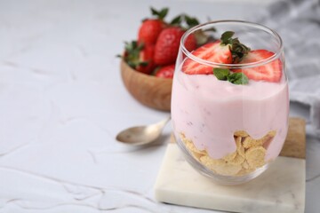 Glass with yogurt, strawberries and corn flakes on white textured table, closeup. Space for text