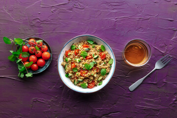 Quinoa tabbouleh salad in a bowl, a healthy dinner with tomatoes and mint, overhead flat lay shot on a purple background with copy space