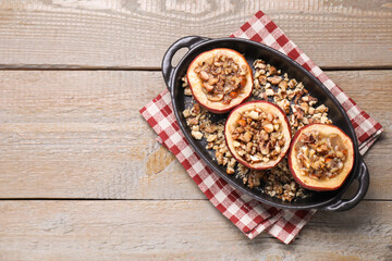 Tasty baked apples with nuts and honey in baking dish on wooden table, top view. Space for text