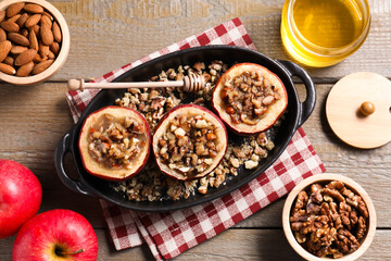 Tasty baked apples with nuts and honey in baking dish on wooden table, flat lay