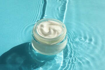 Jar with moisturizing cream in water on light blue background