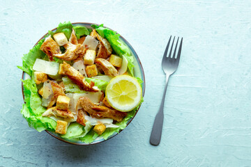 Caesar salad with chicken breast, lettuce, croutons, and a lemon, overhead flat lay shot on a slate background, with copy space