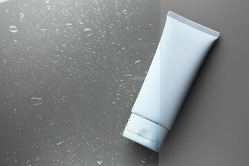 Tube with moisturizing cream on wet grey surface, top view. Space for text