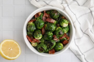 Delicious roasted Brussels sprouts, bacon and lemon on white tiled table, top view