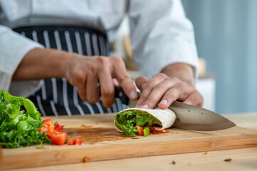 chef make tortilla wrap vegetable salad slice by knife on cutting board and mix sour salad dressing in small bowl glass with wine and olive oil. tortillas wrap vegetable and juicy liquid sour dressing