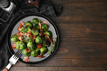 Delicious roasted Brussels sprouts and bacon on wooden table, top view. Space for text