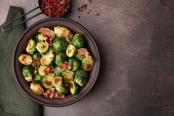 Delicious roasted Brussels sprouts, bacon and peppercorns on brown table, top view. Space for text