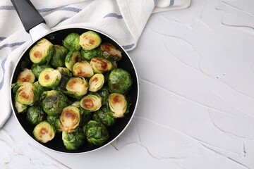Delicious roasted Brussels sprouts in frying pan on white textured table, top view. Space for text