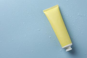 Moisturizing cream in tube on light blue background with water drops, top view. Space for text