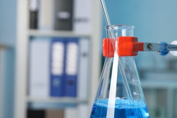 Laboratory analysis. Glass flask with blue liquid on stand indoors, closeup. Space for text