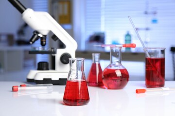 Laboratory analysis. Glass flasks with red liquid and microscope on white table indoors