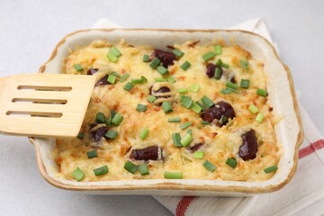 Tasty sausage casserole with green onions in baking dish on white table, closeup