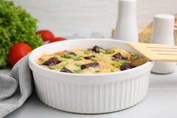 Tasty sausage casserole with green onions in baking dish served on white tiled table, closeup