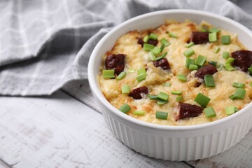 Tasty sausage casserole with green onion in baking dish on white wooden table, closeup. Space for text