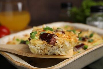 Taking piece of tasty sausage casserole from baking dish at table, closeup