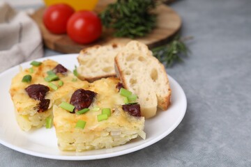 Tasty sausage casserole with green onion and bread on grey table, closeup