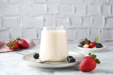 Tasty yogurt in glass and berries on white marble table