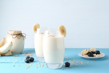 Tasty yogurt in glasses, oats, banana and blueberries on light blue wooden table
