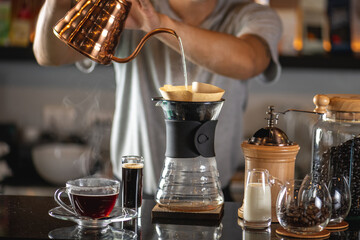 drip coffee, Barista making drip coffee by pouring spills hot water on coffee ground with prepare filter from copper pot to glass transparent chrome drip maker on wooden table in cafe shop - Powered by Adobe