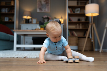 Young happy adorable baby girl or boy sitting on the floor of apartment playing with his or her...