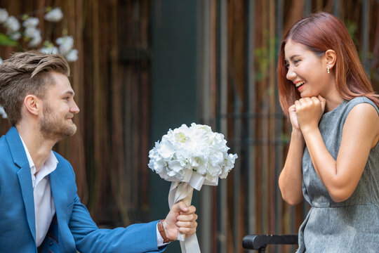 Lover propose marriage hide white rose in hands for surprise romantic date at valentine. Two lover holding rose symbol for show love and propose marriage with asian woman.