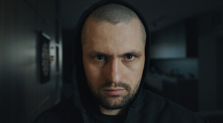 Front view portrait of a brutal man looking intently at the camera from under a black hood. Dark...