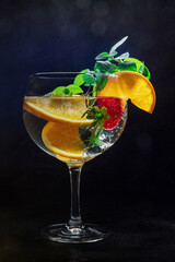 Fancy cocktail with fresh fruit. Gin and tonic drink with ice at a party, on a black background. Alcohol with orange, mint, and strawberry, toned image