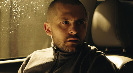 Portrait of adult handsome dark-haired man looking in shock, standing in the dark car inside.