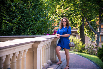 Beautiful young smiling woman in sunglasses in city park at summer day wearing dress and looking to the camera