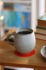 Cup of tea or coffee, pile of books, plate of cookies, reading glasses, e-reader and pen on the table. Colorful rainbow bookshelf in the background. Selective focus.