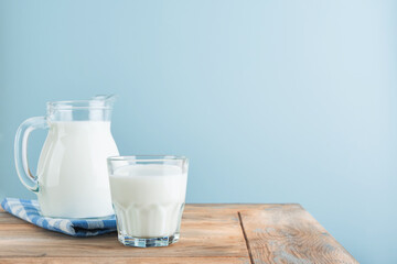 Milk in jug and glass on wooden table and blue background. Concept of farm dairy products, milk day. Kitchen or supermarket mock up for design. Copy space.