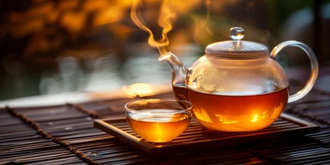 Raamstickers A transparent teapot with hot tea and a cup, emanating warmth in a cozy evening ambiance. © tashechka