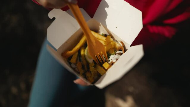 Person holding box of food with fork, enjoying comfort cuisine