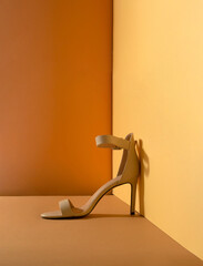 Minimal concept of women's beige sandal with a high heel placed in the corner. Sustainable fashion on yellow and brown background.