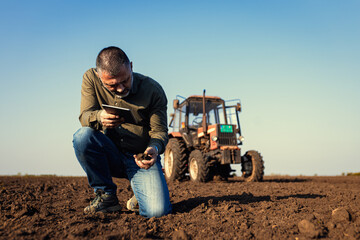 Portrait of satisfied mature farmer standing in field with tablet supervises the cultivation of soil.