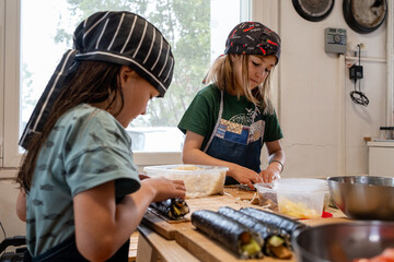 twin sisters dressed in their aprons and hats preparing sushi in the kitchen, roll up and put the rice with vegetarian makis.