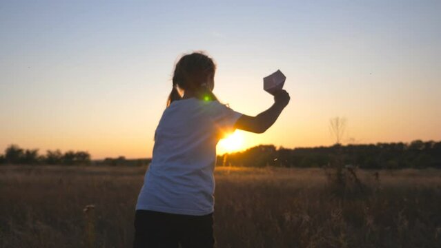 Carefree little child jogging with toy plane among meadow over sunset background. Happy small girl running with a paper airplane through grass field. Cute kid having fun at nature. Childhood dream