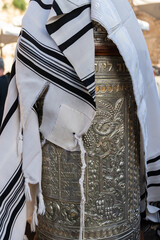 A tallit or Jewish prayer shawl draped over the silver case enclosing a Sefardi style Torah scroll.