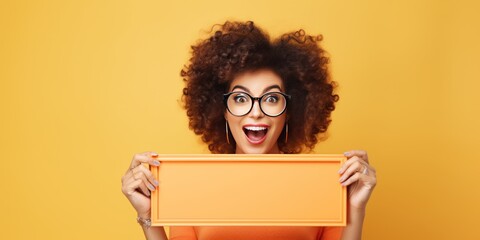 Photo of A woman holding up an empty frame with space for text on violet background, excited expression, wearing sunglasses and yellow dress - obrazy, fototapety, plakaty