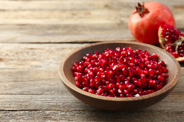 Ripe juicy pomegranate grains in bowl on wooden table. Space for text
