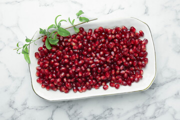 Ripe juicy pomegranate grains and green leaves on white marble table, top view