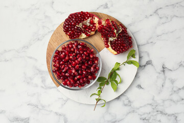 Ripe juicy pomegranate grains and green leaves on white marble table, top view
