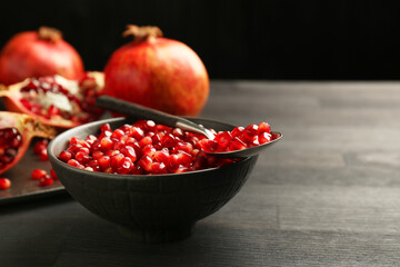 Tasty ripe pomegranates and grains on dark wooden table, closeup. Space for text
