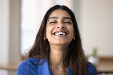 Happy relaxed carefree Indian woman laughing with closed eyes, showing perfectly white healthy teeth, smiling, posing indoors. Cheerful young 20s girl enjoying positive emotions